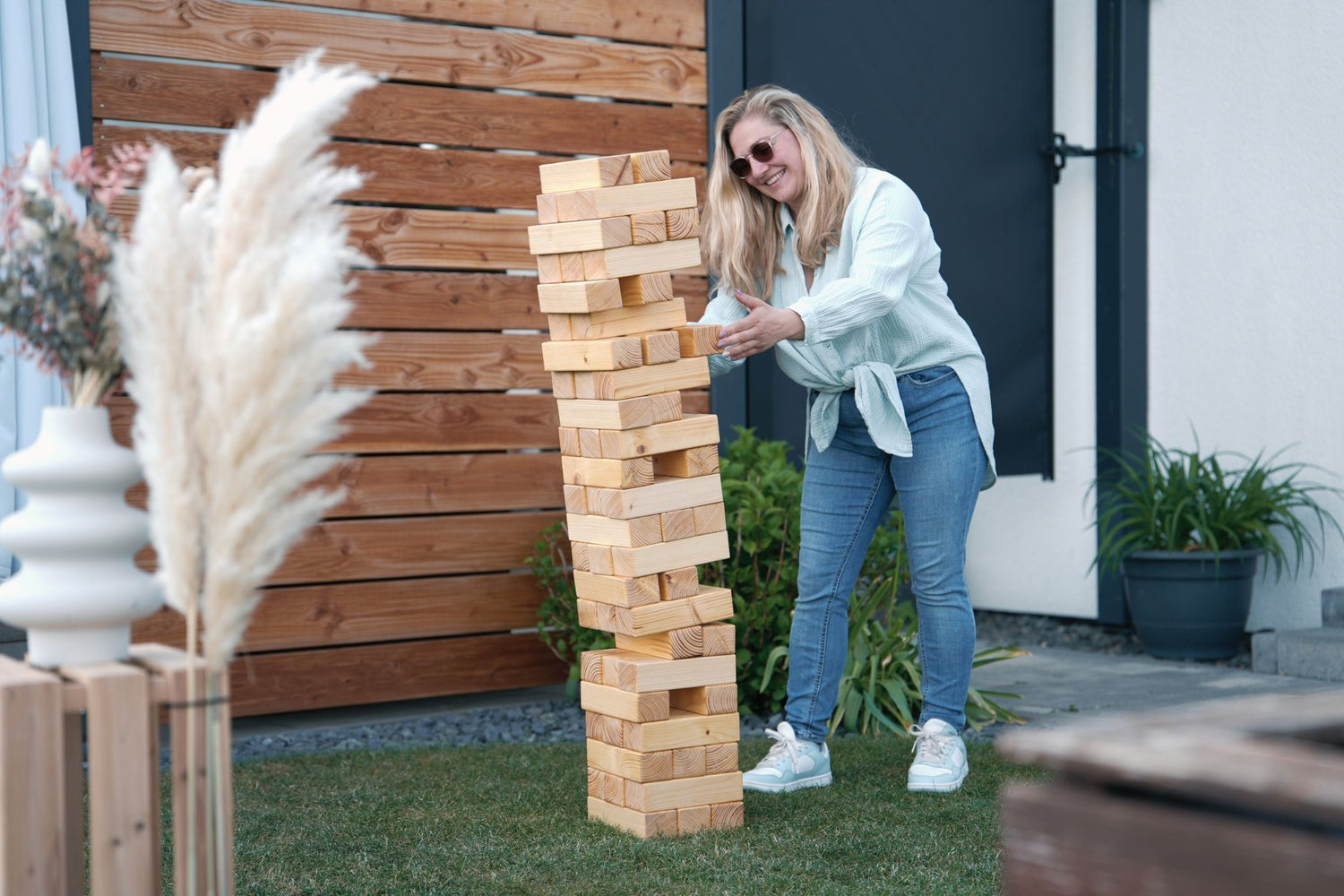XXL Jenga Spiel aus Holz für Gartenparty – Frau spielt riesiges Outdoor-Geschicklichkeitsspiel bei Event